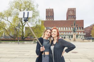 Two beautiful young women taking a selfie in Oslo with a selfie stick. They are on their mid twenties, caucasian, with nordic features. Lifestyle and friendship concepts.