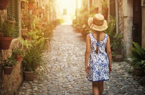 Little girl walking down beautiful street of a mediterranean town. The girl is wearing a sundress and straw hat.
